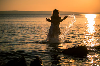 Woman in sea against sky during sunset