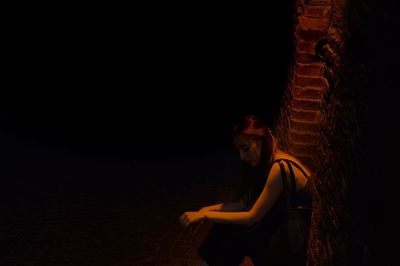 Sad young woman sitting by wall at night