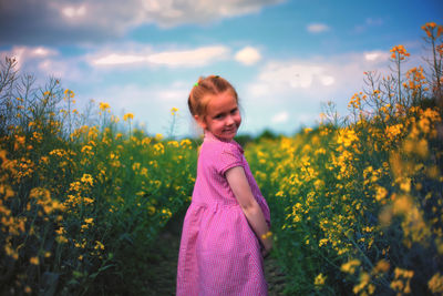 Portrait of smiling girl standing on field against sky