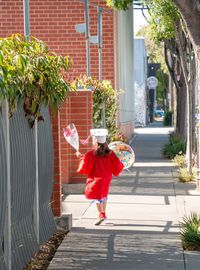 Rear view of girl wearing graduation gown walking on footpath against buildings in city