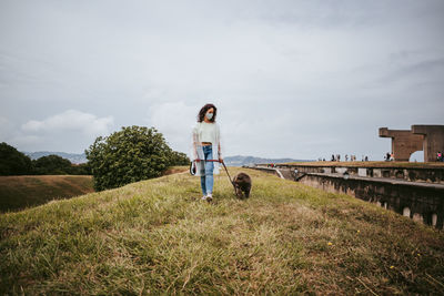 Woman with dog walking on grass against sky