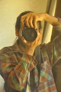 Waist-up of a man looking through the viewfinder of his dslr camera taking photo of itself.