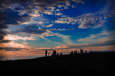 Silhouette people on beach against sky during sunset