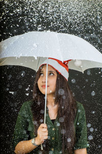 Young woman with umbrella during snowfall against black background