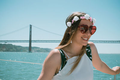 Smiling young woman wearing sunglasses standing against clear sky during sunny day