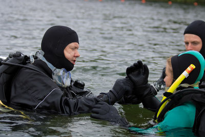 Man assisting woman for wearing gloves while swimming in sea