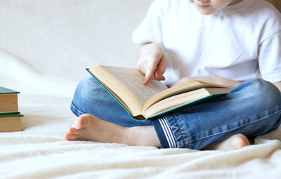 A child in blue jeans sits on the bed and holds an open book in his hands. home leisure.