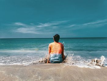 Rear view of man sitting on beach against sky