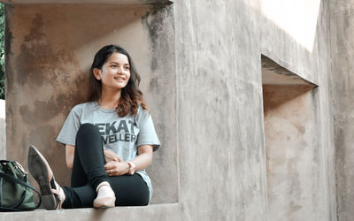 Portrait of smiling young woman sitting on wall