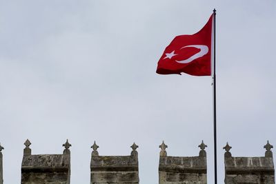 Low angle view of turkish flag by historic building against sky