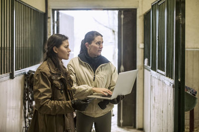 Women using laptop in horse stable