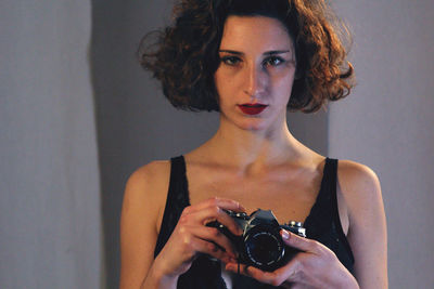 Portrait of beautiful woman holding camera against wall