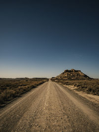 Dirt road amidst desert against clear sky