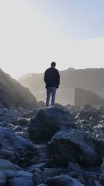 Rear view of man standing on rock against sky