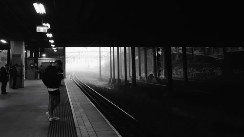 Passengers standing at illuminated railroad station platform during foggy weather