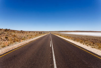 Road passing through landscape against clear blue sky