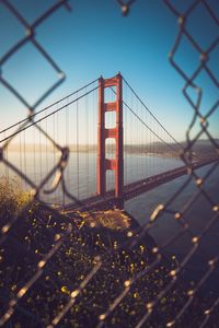 View of suspension bridge against sky through fence 