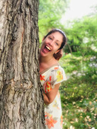 Portrait of smiling young woman standing against tree trunk