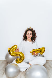 Full length of woman holding balloons sitting on floor against white backgrounds