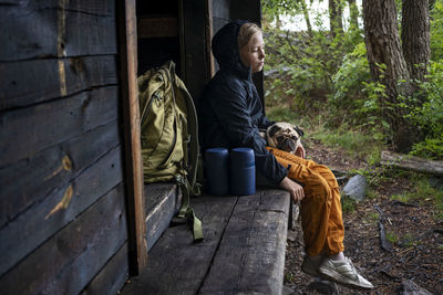 Girl with pug sitting by wooden building