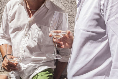 Midsection of friends drinking white wine during wedding