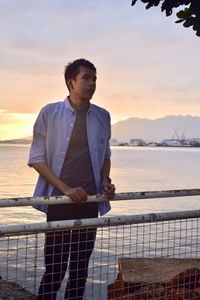 Man standing by railing against sea during sunset