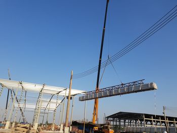 Low angle view of cranes against clear blue sky