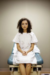 Portrait of woman with hands clasped sitting on bed in hospital