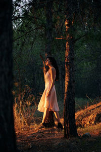 Woman standing by tree trunk in forest