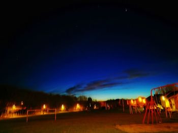 Illuminated road by silhouette trees against sky at night