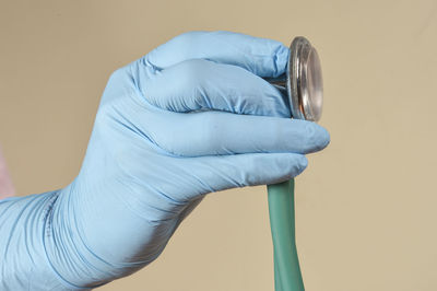Hand with protective gloves holding medical object in a light brown background