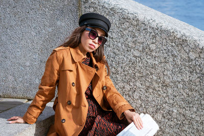 Young woman sits on the steps on the embankment with newspaper in hand