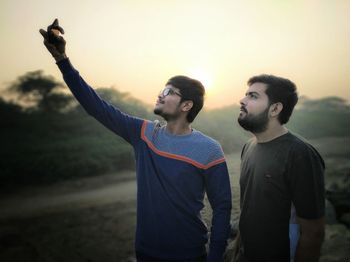 Male friends taking selfie while standing on field against clear orange sky