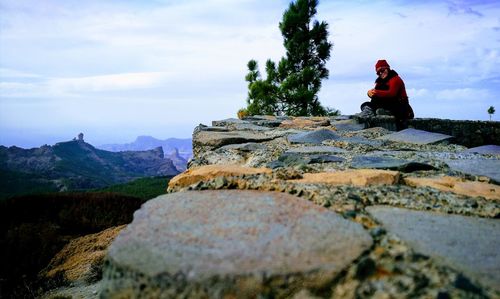 Surface level of woman sitting on stone wall against sky