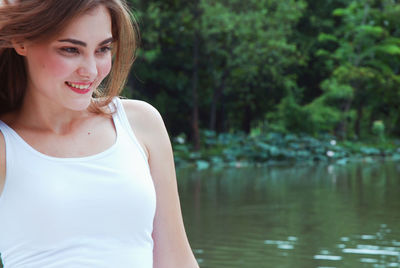 Smiling young woman standing against lake in park
