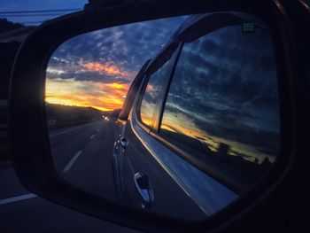 Close-up of side-view mirror against sunset sky