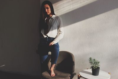 Portrait of young woman standing against wall at home