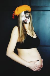 Pregnant woman with painted face standing at home during halloween