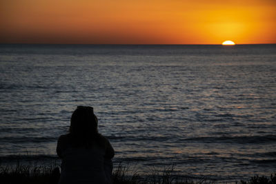 Rear view of man looking at sea against sky during sunset