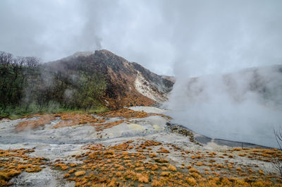 Scenic view of mountain by hot spring against sky