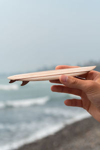 Cropped hand of person holding small surfboard against sky