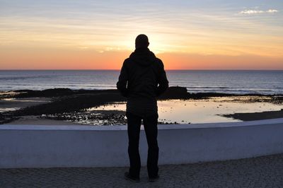 Rear view of man standing on beach at sunset