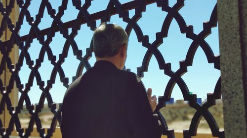 Rear view of woman standing by fence against sky