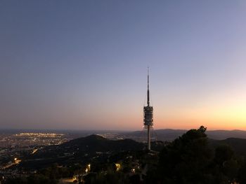 Communications tower in city against sky during sunset