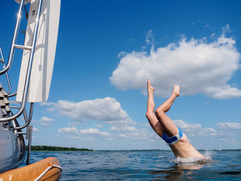 Young person jumping from a sailboat stern into the water, view from water person
