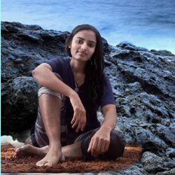 Portrait of a young woman sitting on rock by sea