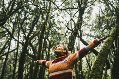 Carefree woman standing with arms outstretched in forest