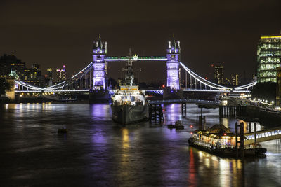 Illuminated bridge over river in city at night