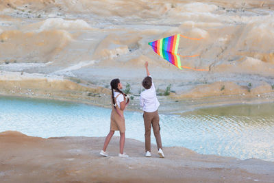 A boy and a girl launch a bright kite mountains near the river.