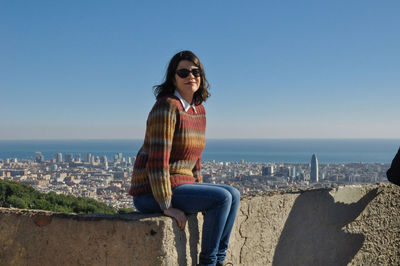 Portrait of young woman against sea and cityscape against sky